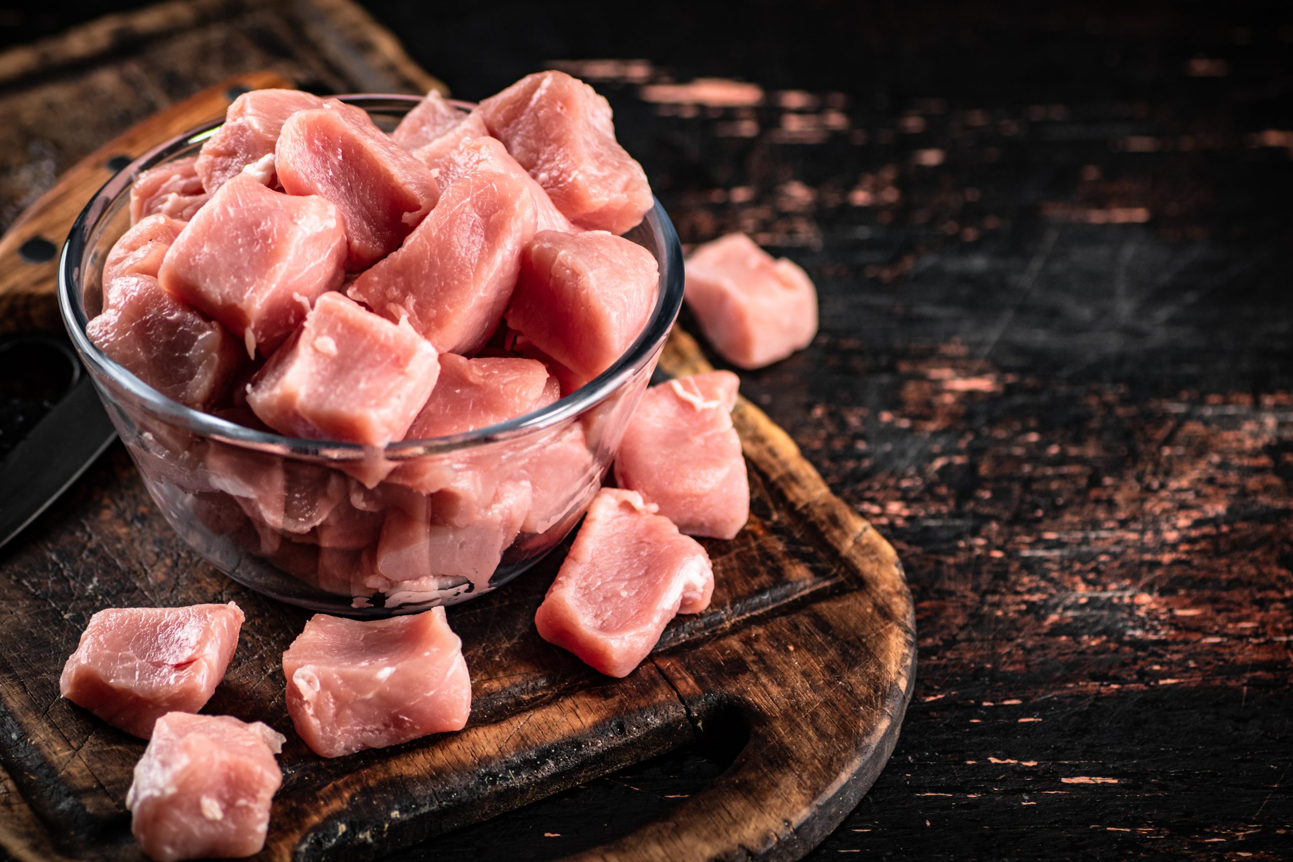 Pieces of raw pork in a bowl on a cutting board. Against a dark background. High quality photo